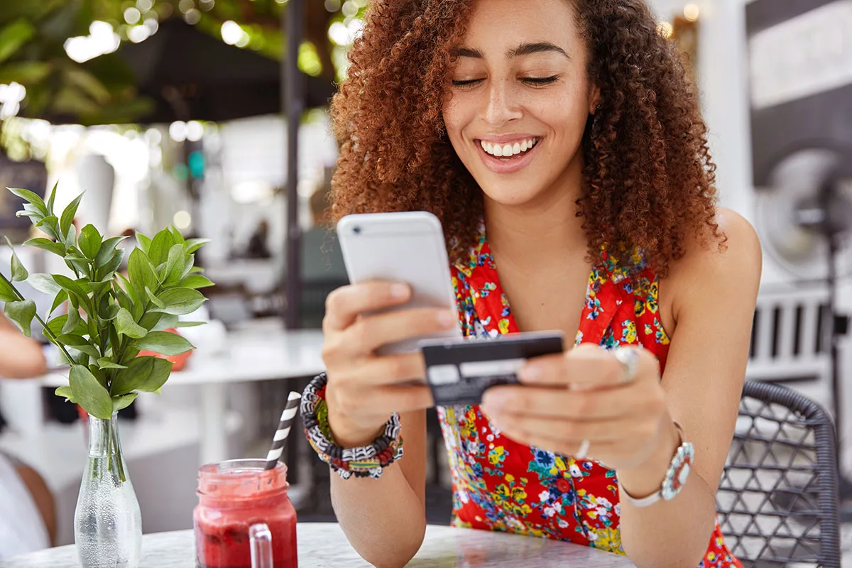 Woman shopping online with phone and credit card at cafe
