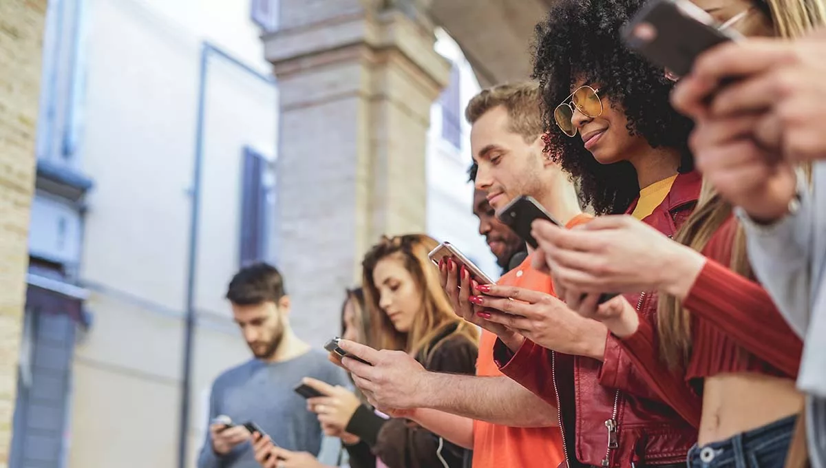 Group of diverse young adults using smartphones outdoors