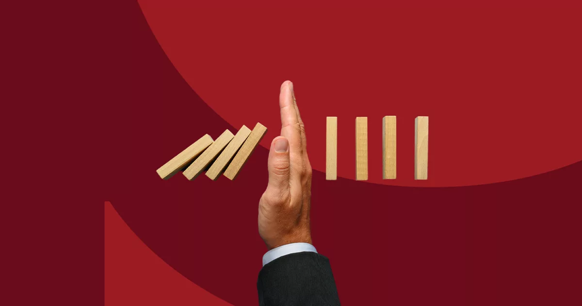 Hand stopping falling dominoes on red background