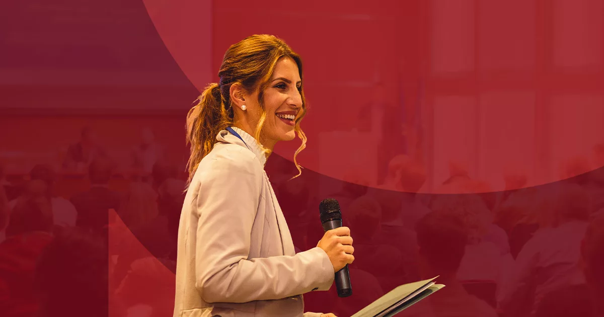 Woman in white blazer speaking into a microphone on stage