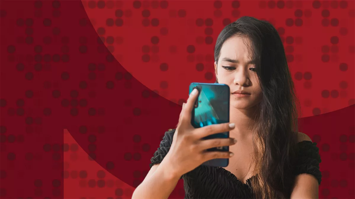 Woman in black dress looks at smartphone against a red dotted background.