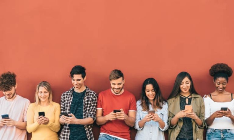 Group of diverse friends using smartphones against a vibrant orange wall, showcasing modern social connection and technology.