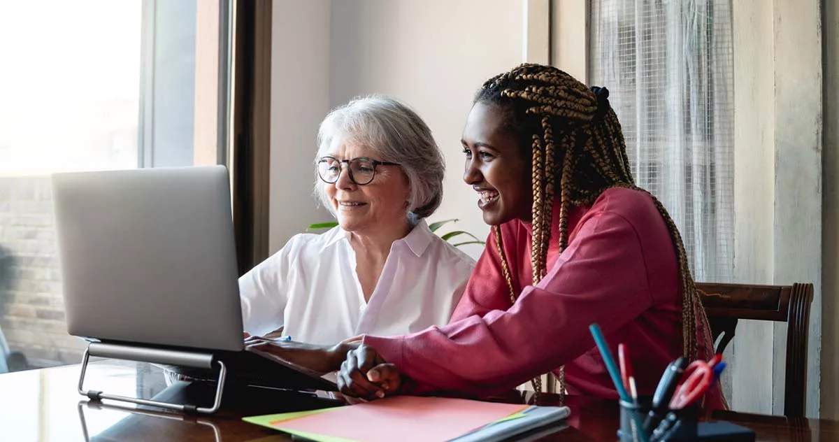 Two women smiling while using a laptop together