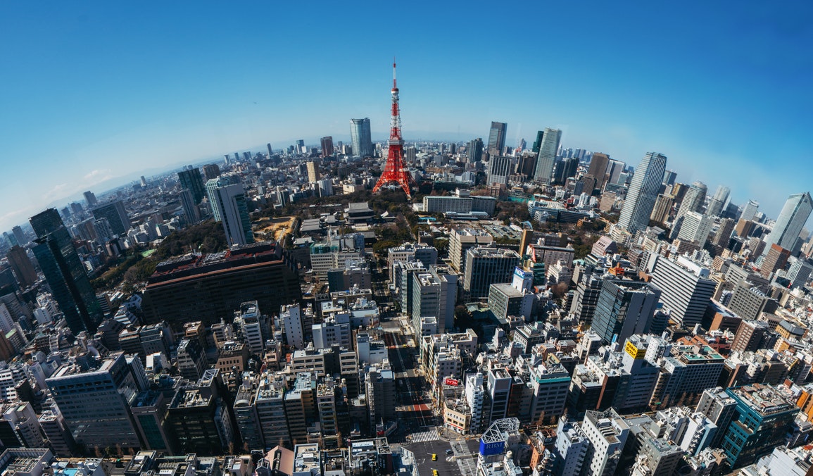 Aerial view of Tokyo skyline featuring the iconic red Tokyo Tower amidst modern skyscrapers under a clear blue sky.