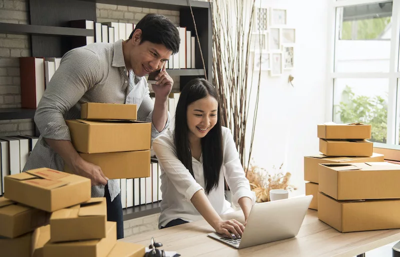 Two people discuss online store orders with stacked cardboard boxes