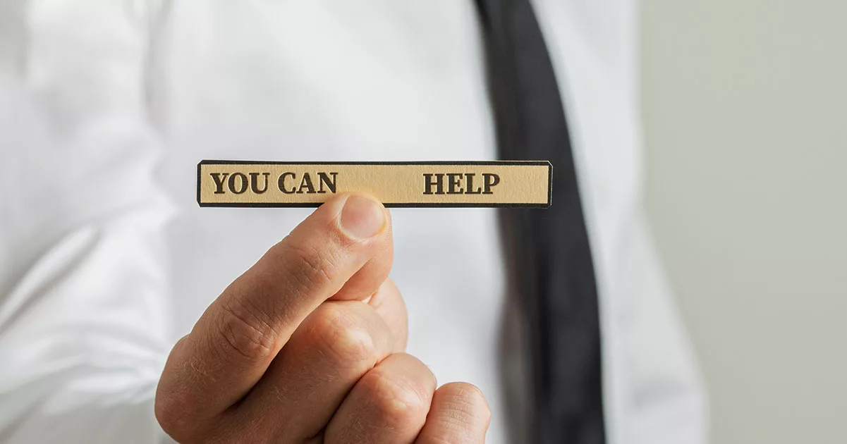 Hand holding a beige card with the text "You Can Help" in focus