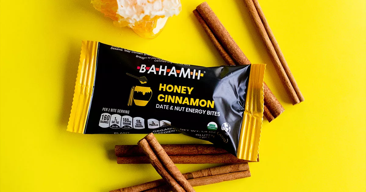 Packet of Bahamii Honey Cinnamon Energy Bites with cinnamon sticks and honey on a yellow background.