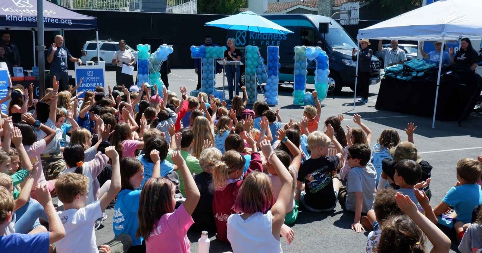 Children sitting down and raising their hands at a Kindness is Free event