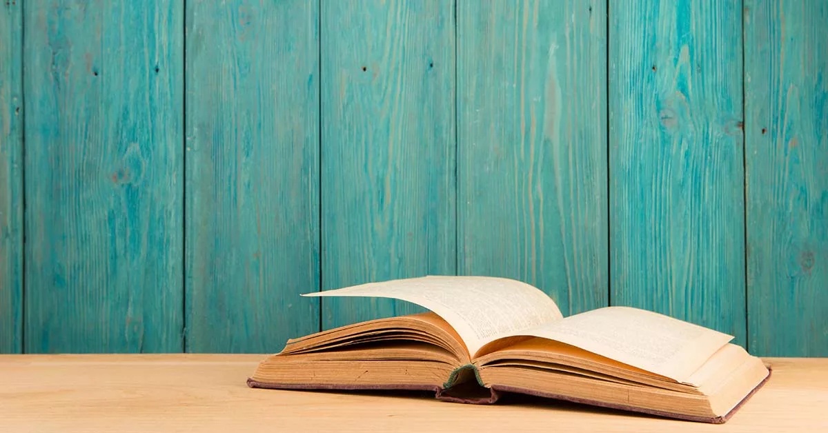 Open book on wooden table against teal wooden background.