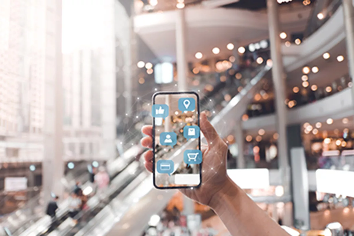 Hand holding smartphone with digital shopping icons in a modern mall