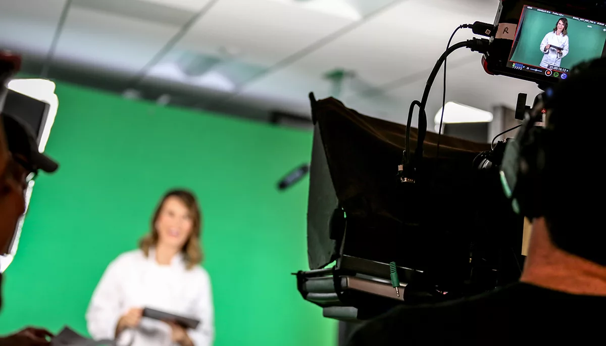 Film crew recording woman with green screen background.