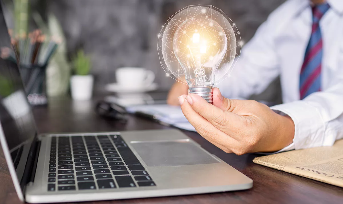 Person holding glowing light bulb near laptop
