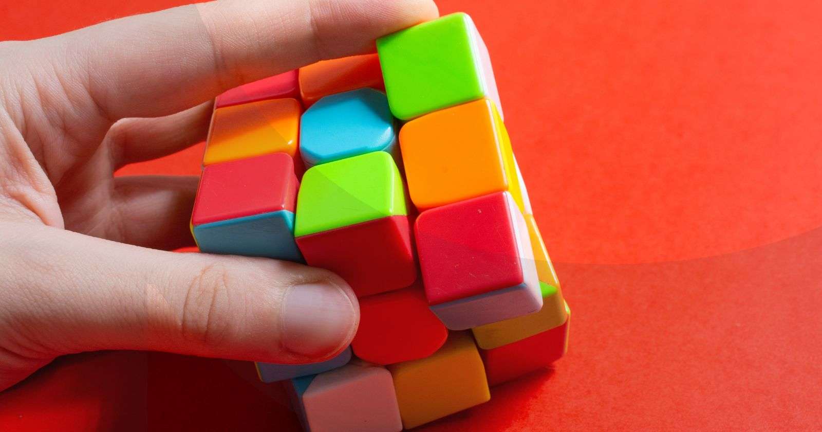 A hand solving a rubik's cube against an orange background.