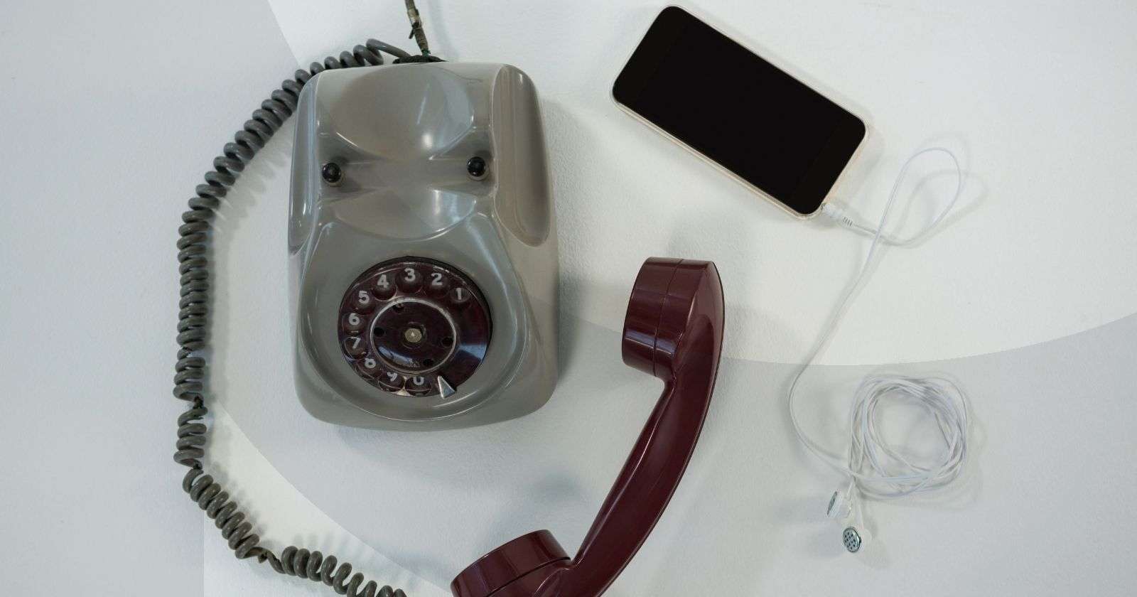 A wired rotary telephone laying next to a smartphone with wired earbuds plugged into it.