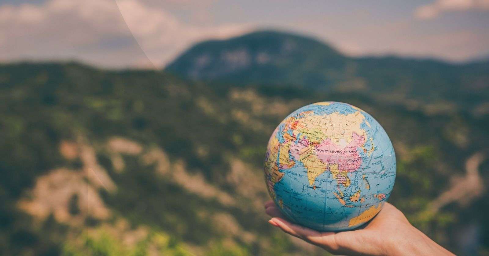Hand holding a small version of a globe in the middle of a forest