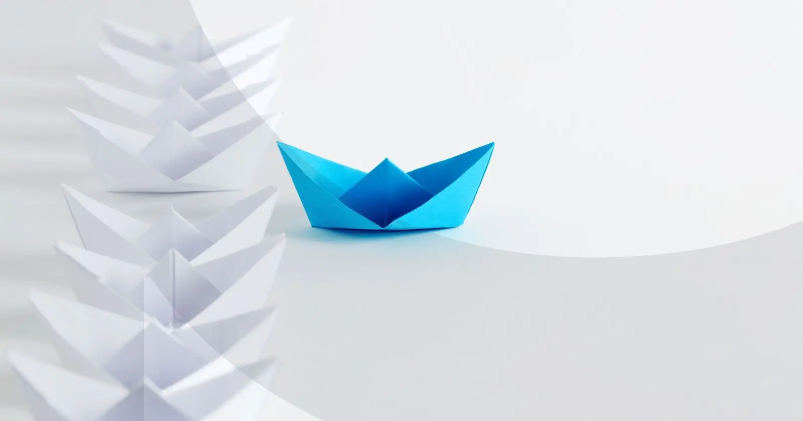 Blue paper boat moving ahead of a line of white paper boats.