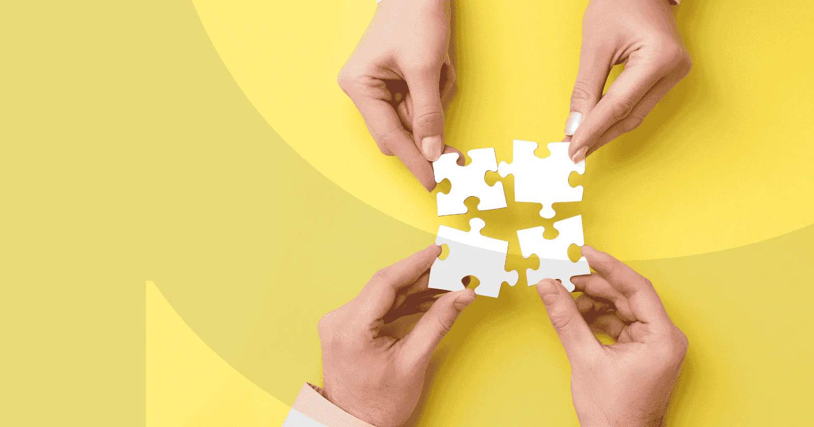 Four hands putting together four puzzle pieces on a yellow background