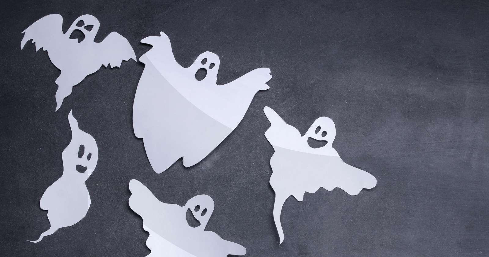 Five cutouts of white ghosts flying against a charcoal background.