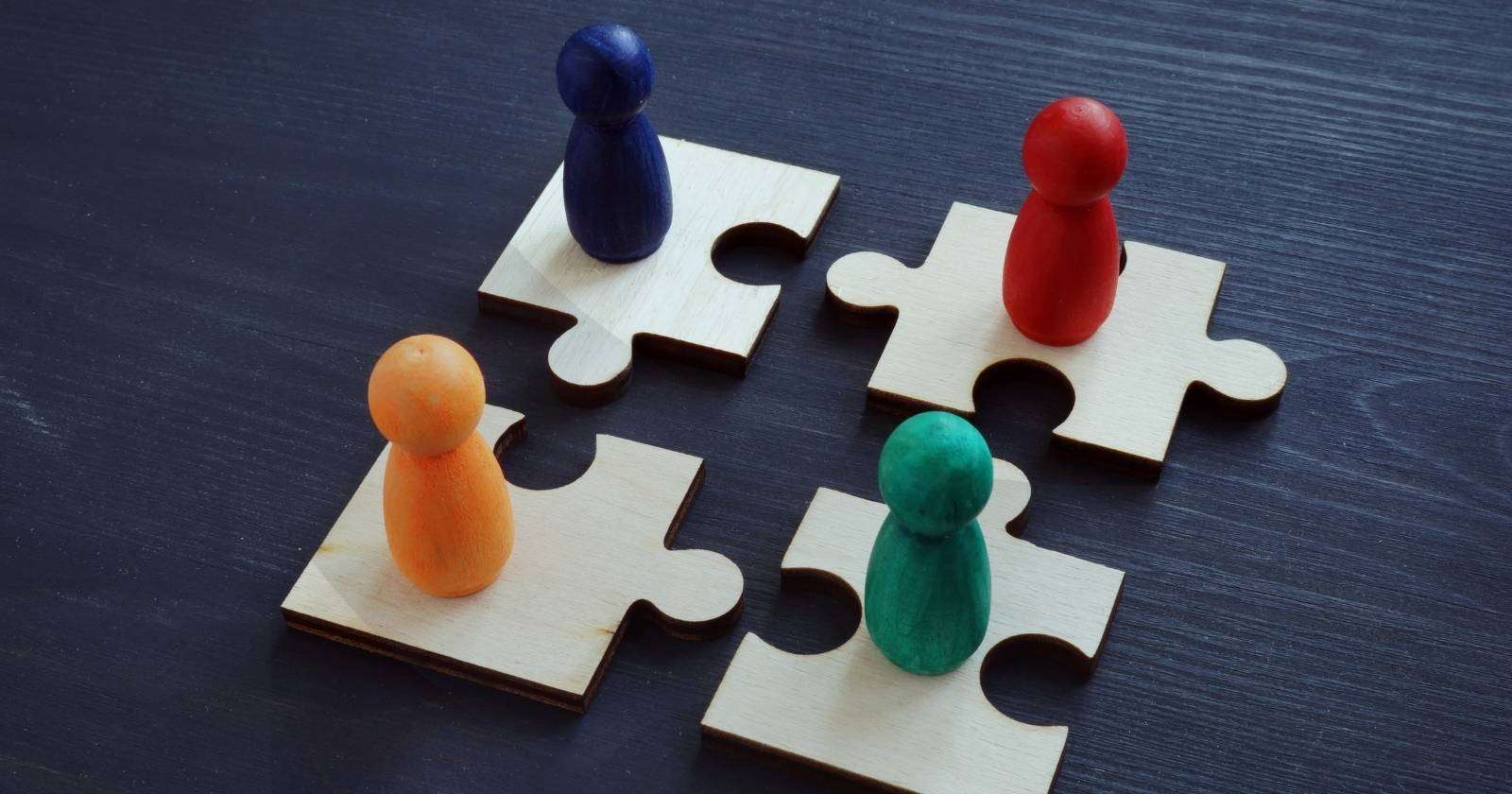 Four jigsaw puzzle pieces with different colored pegs on top of them equally distanced from one another