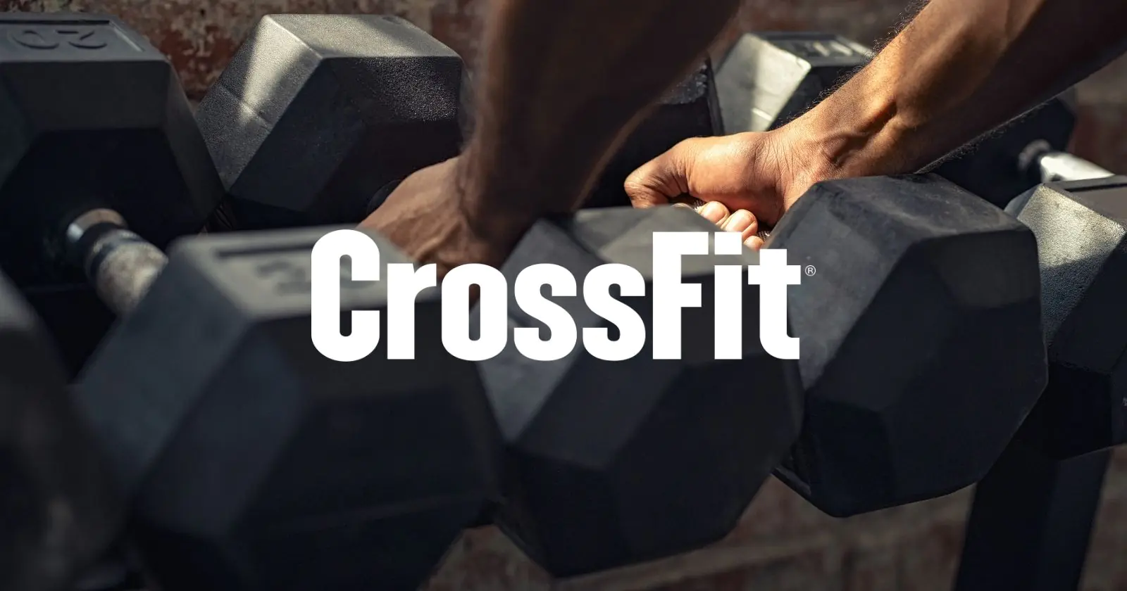 Athlete gripping hex dumbbells during strength training workout at gym with Crossfit logo on top of image