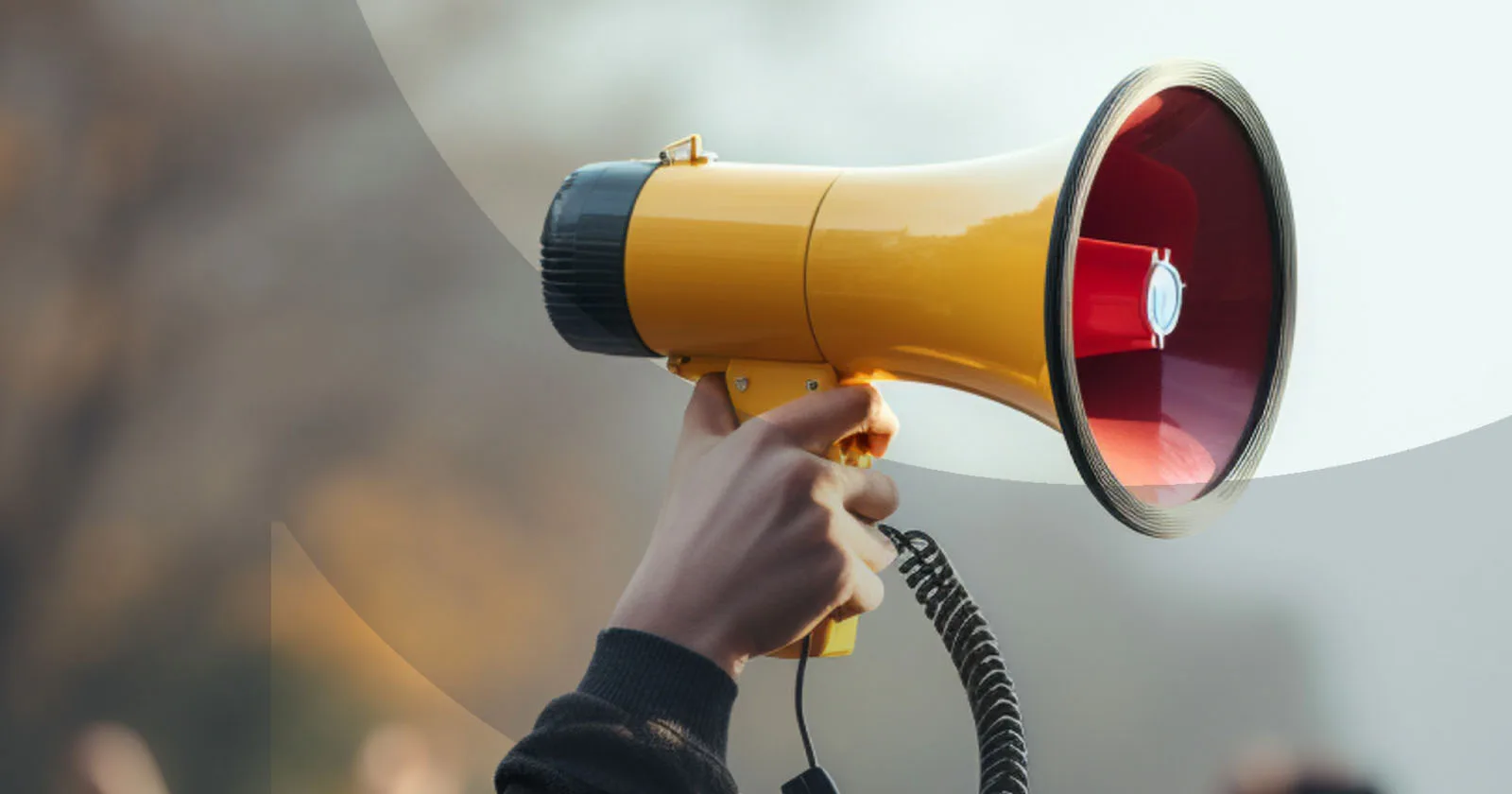Hand holding a yellow megaphone against a blurred background