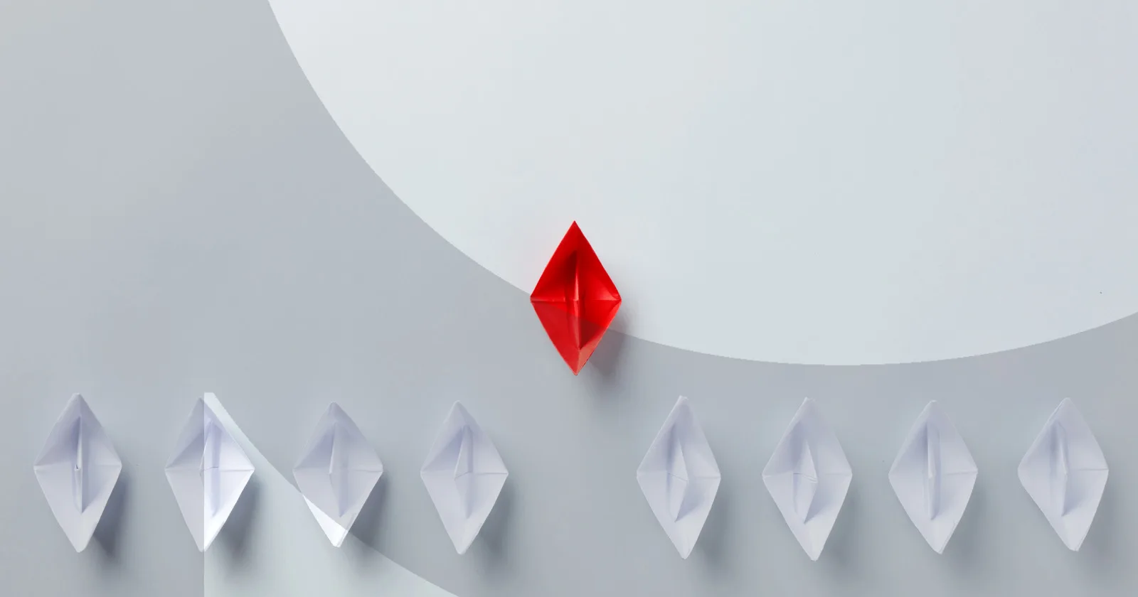 Red origami boat leads white boats on gray background
