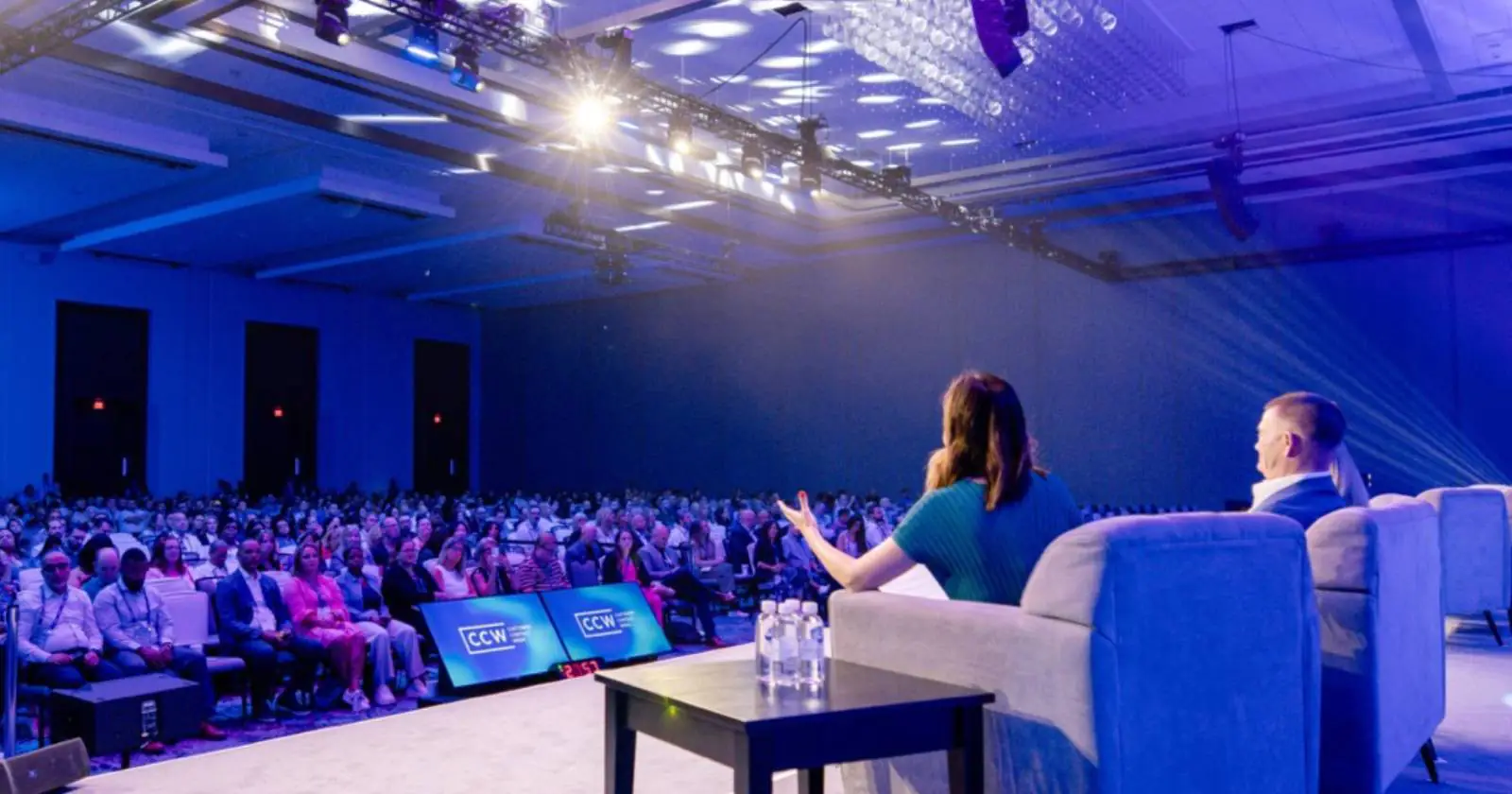 Speakers onstage at a conference addressing a large audience