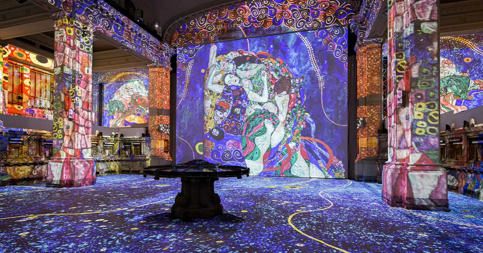 Immersive art exhibit with colorful Klimt projections on walls and columns