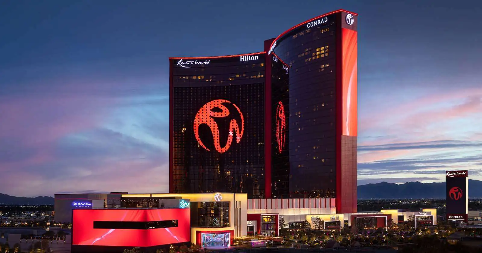 Illuminated Resort World building at dusk with vibrant red lights and mountain backdrop.