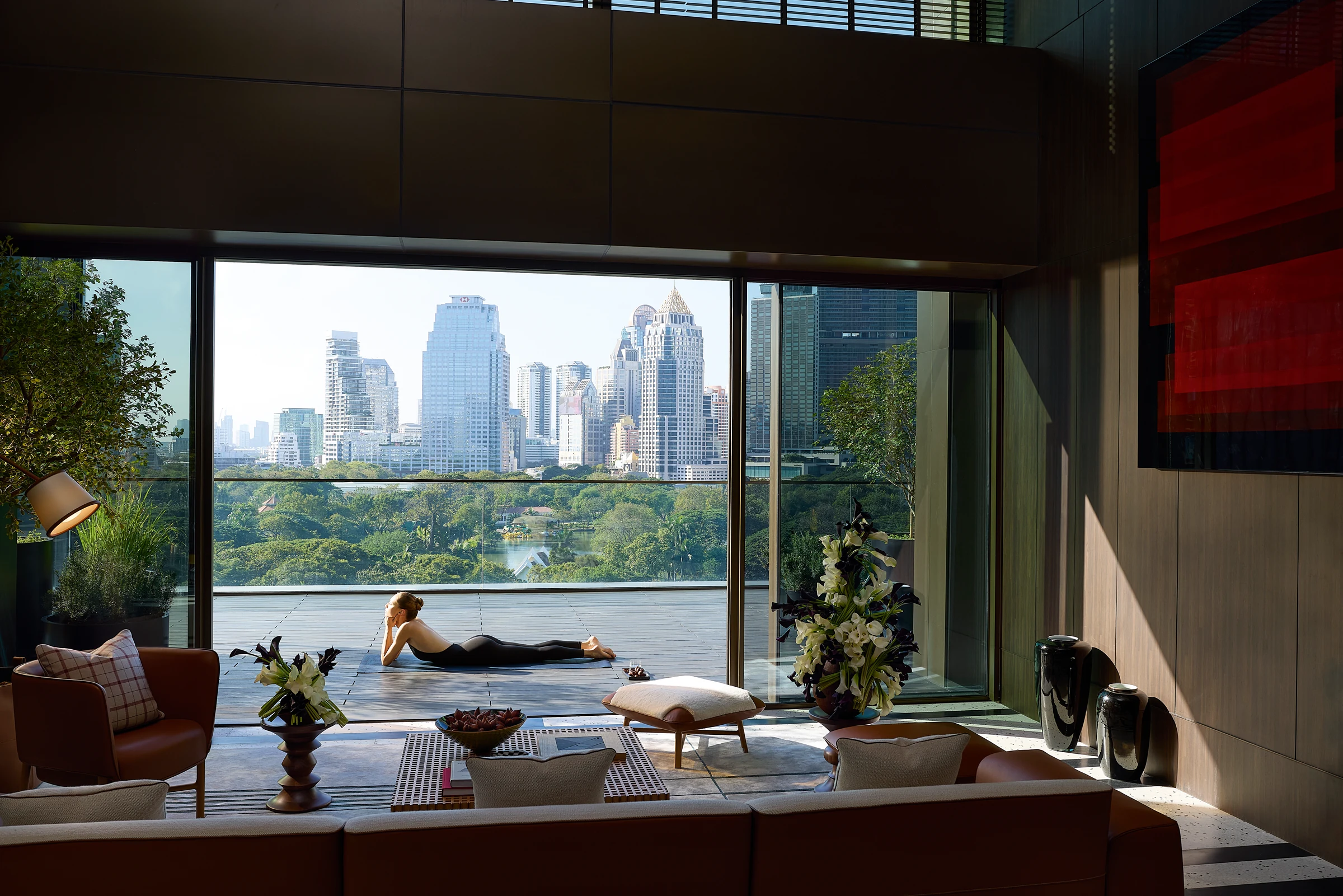 A resident stretching on a terrace beside a lounge overlooking Bangkok and the park.