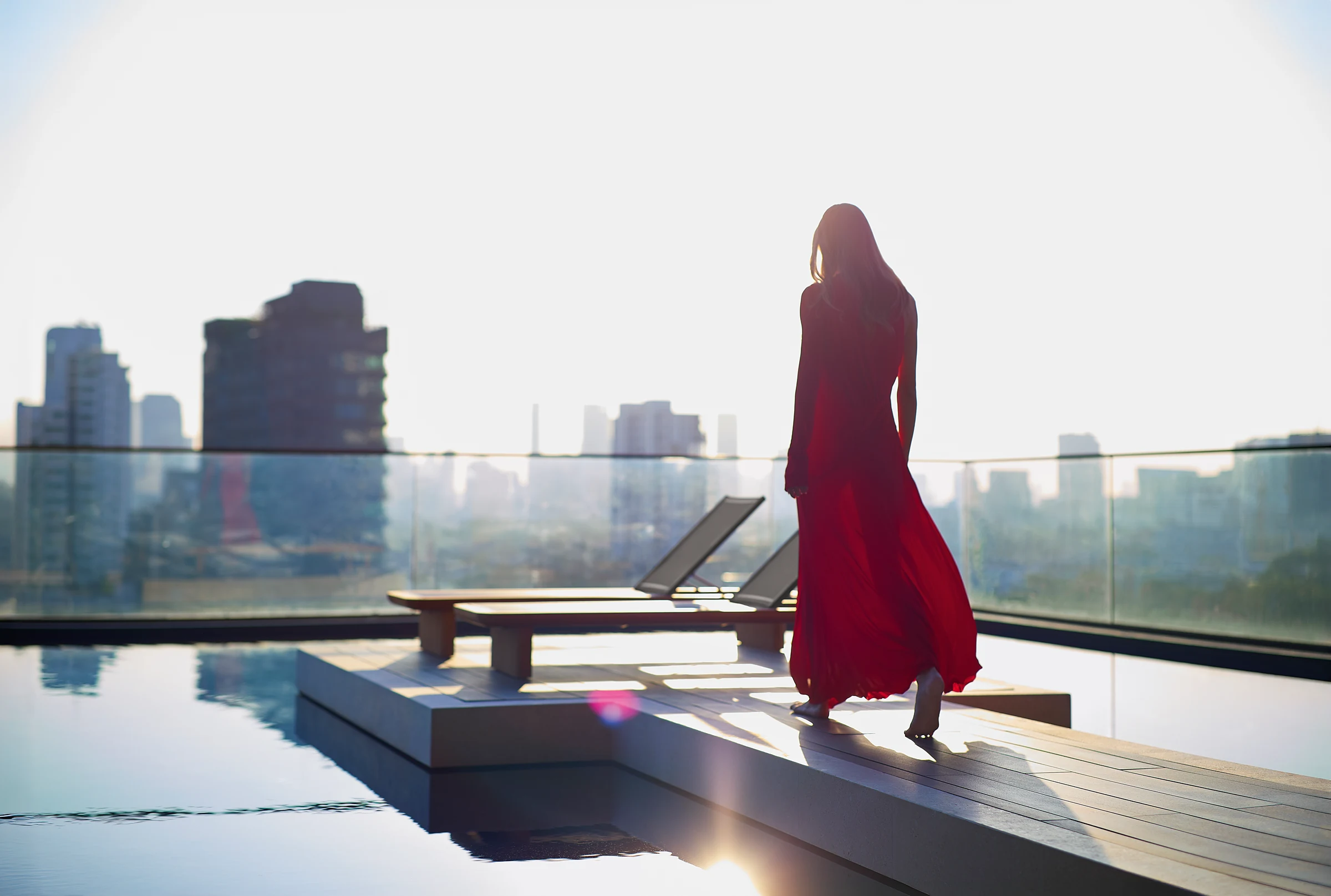 A resident standing beside the outdoor pool with Bangkok beyond.