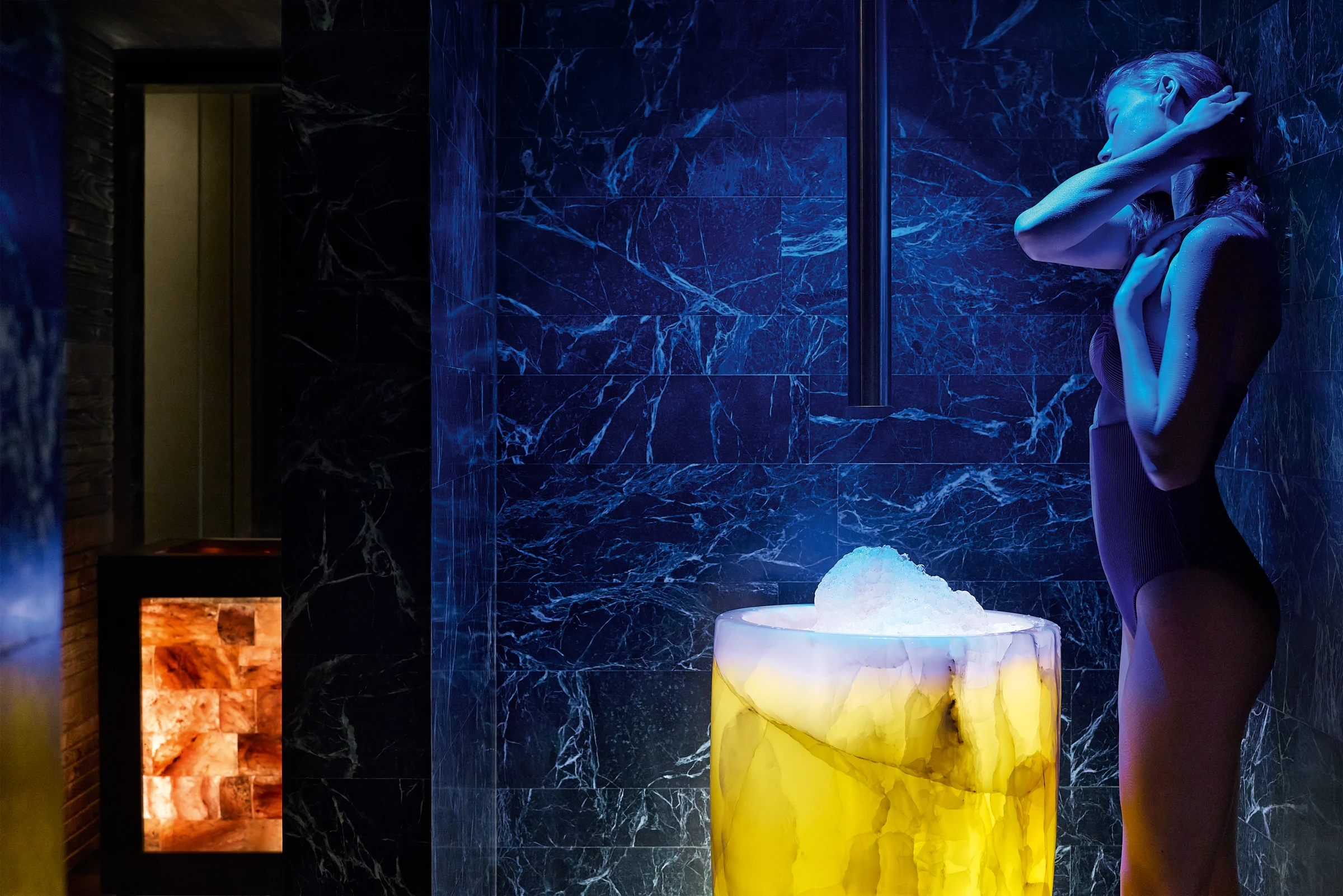 A resident beside an illuminated basin in a dark stone wellness room.