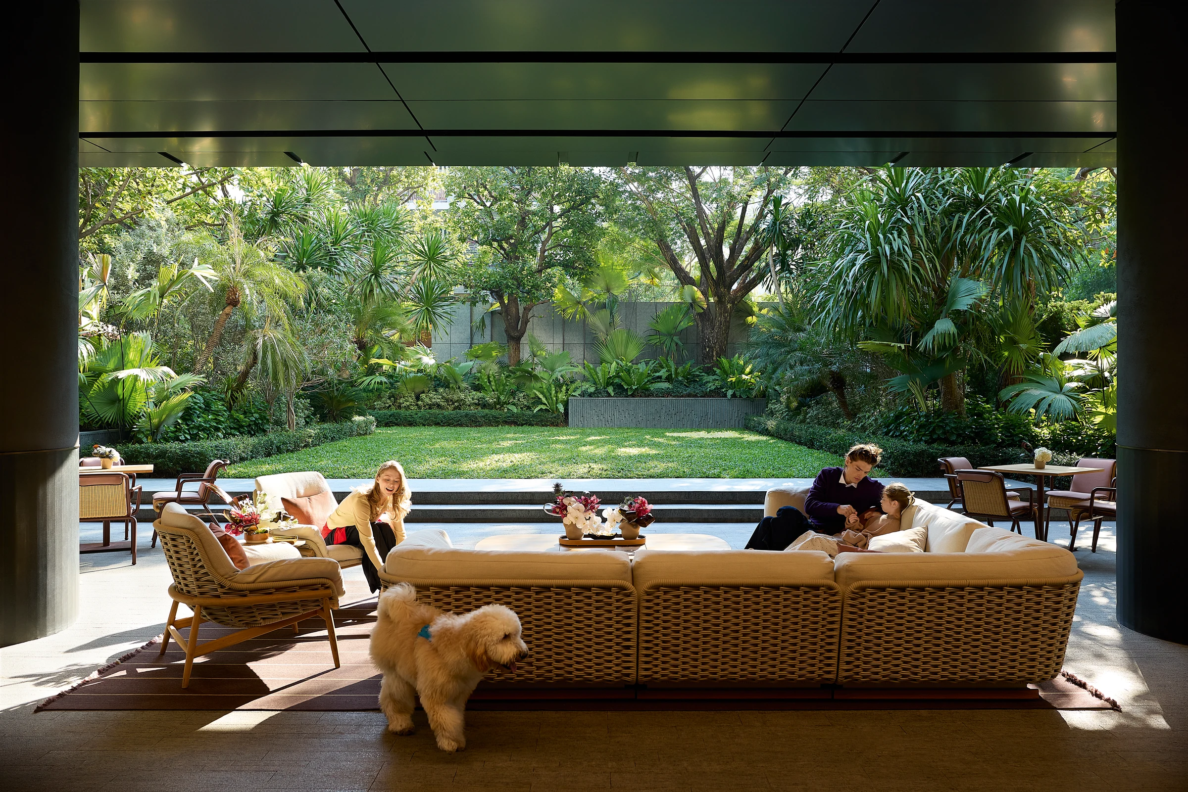 Residents and a dog relaxing in an open lounge beside a landscaped garden.