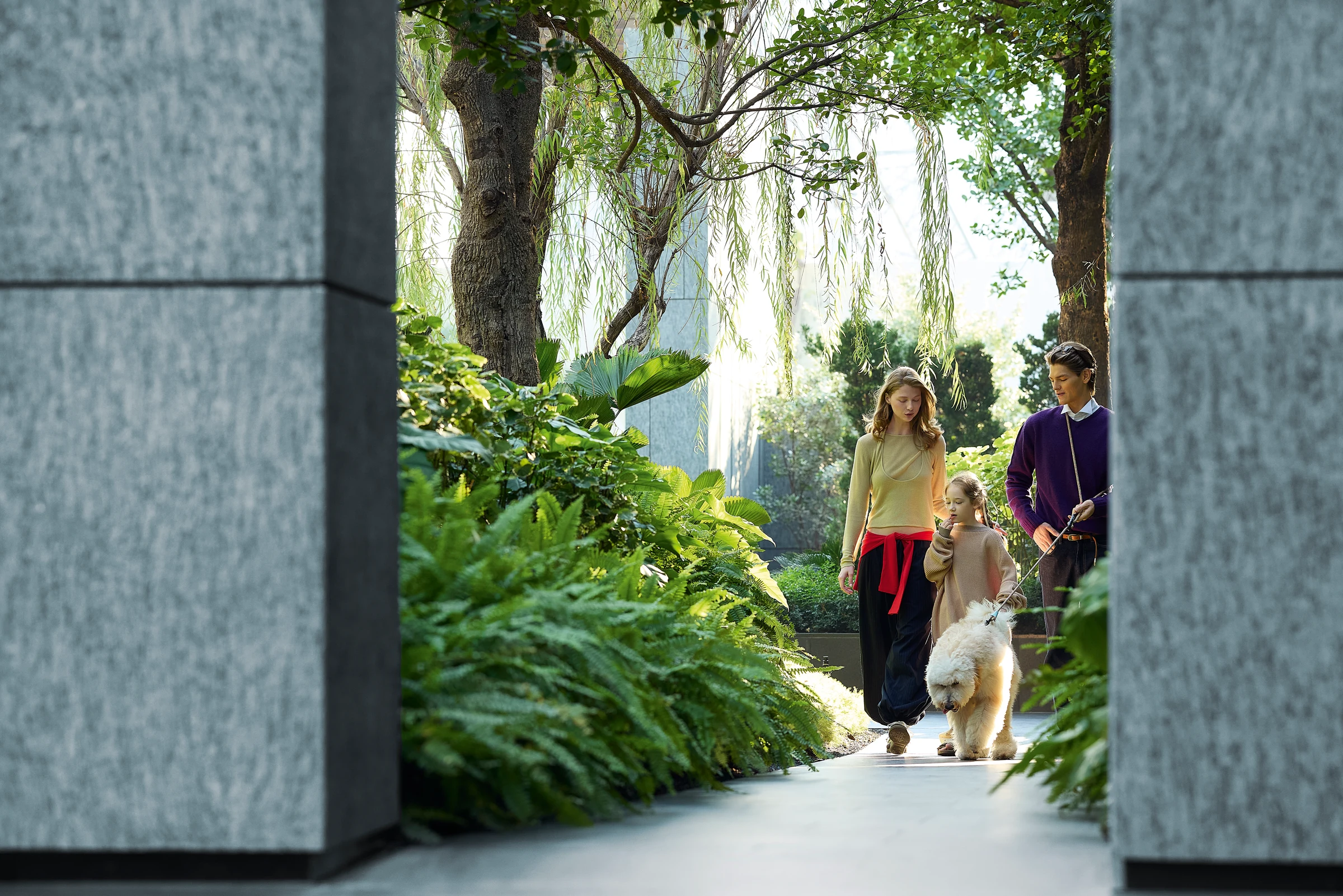 Two people walking a dog through a shaded landscaped passage.