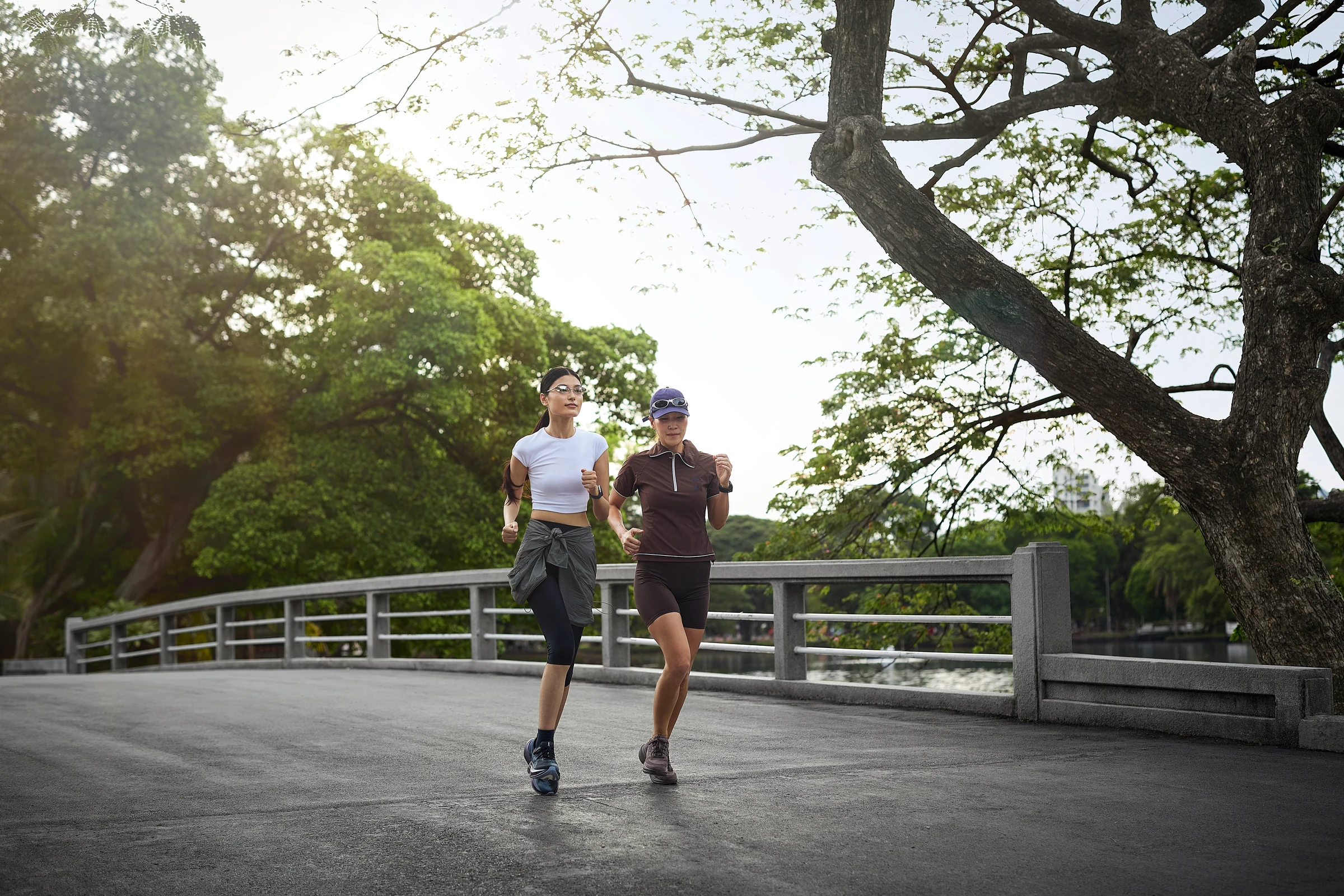 Two people jogging across a tree-lined pedestrian bridge.
