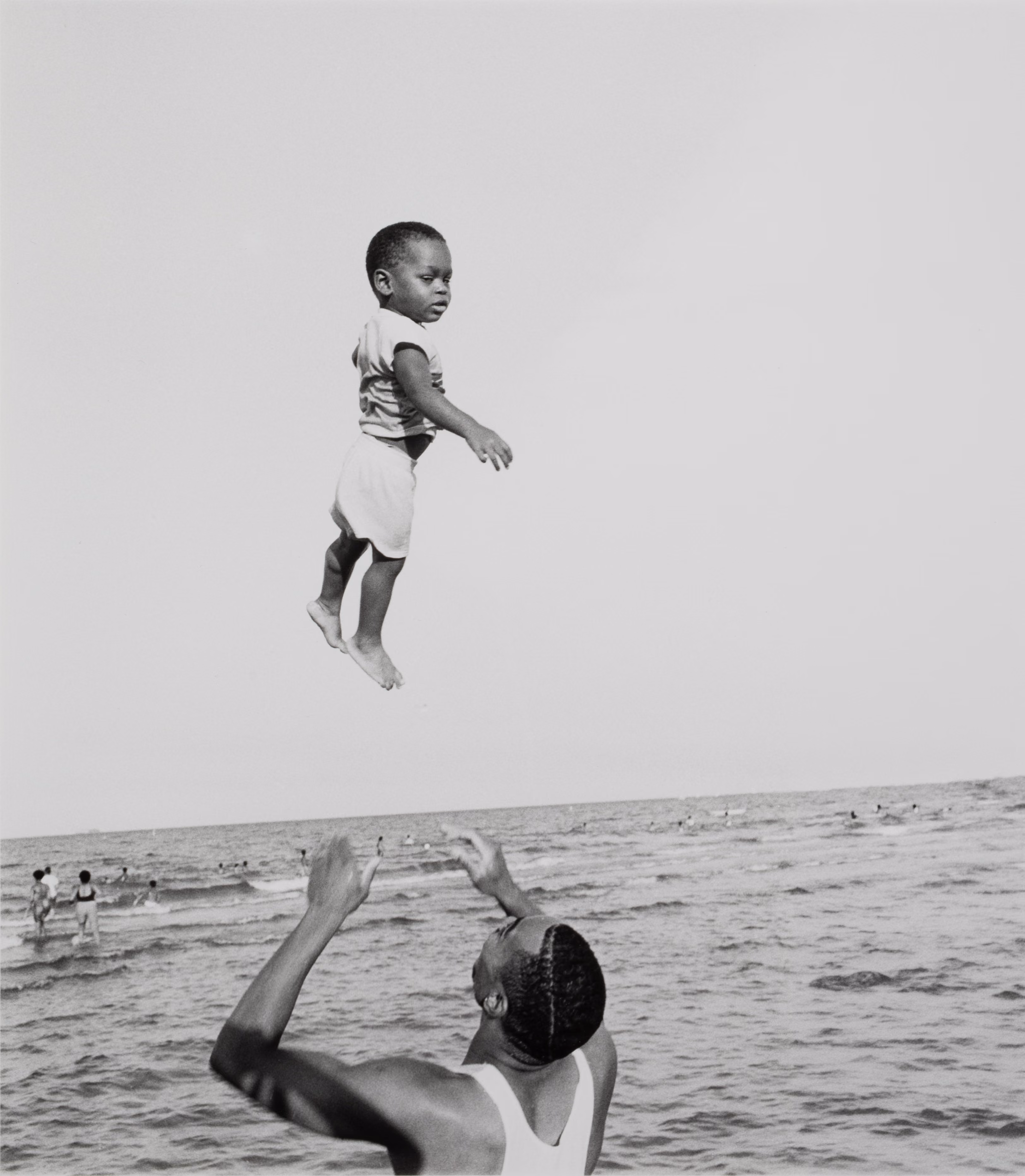 Black-and-white photo by Stephen Marc of a father playfully throwing his son into the air on a beach.