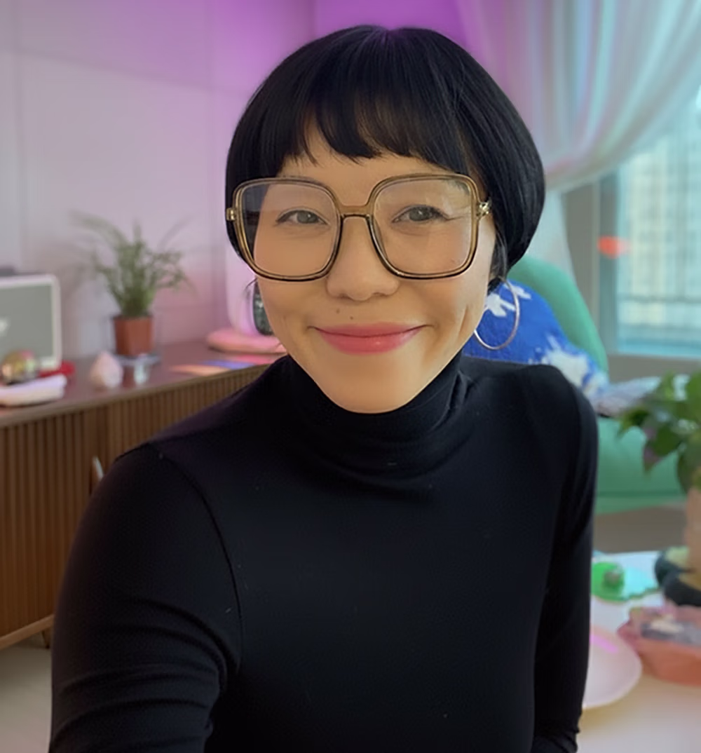 Smiling woman with short black hair, large glasses, and hoop earrings wearing a black turtleneck.