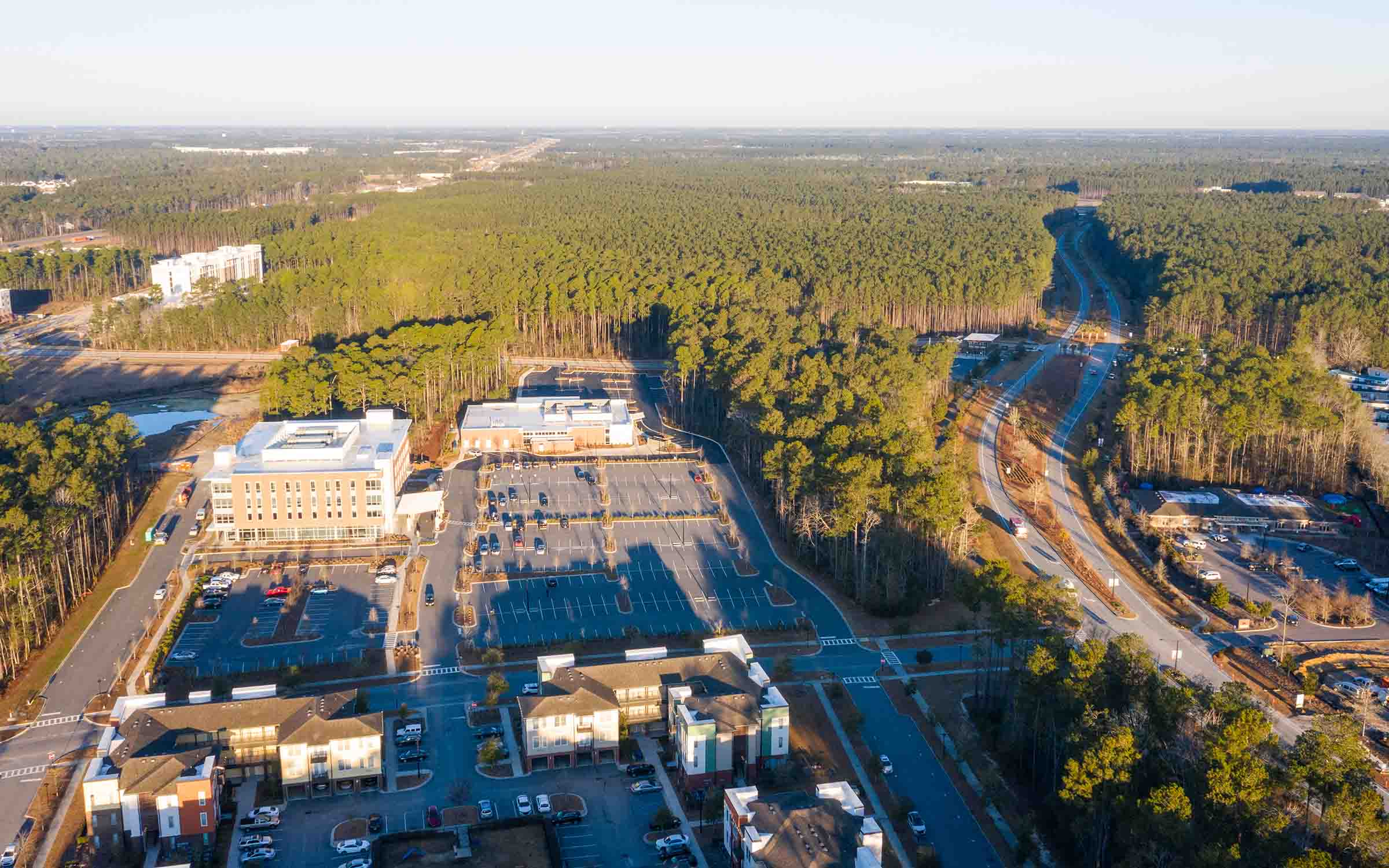 Aerial view of medical office buildings, parking lots, roads, and a large forest area under clear sky.