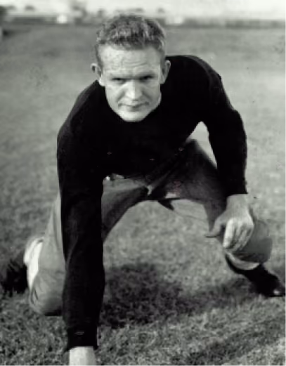 Black and white photo of a football player in a crouched stance on grass field.