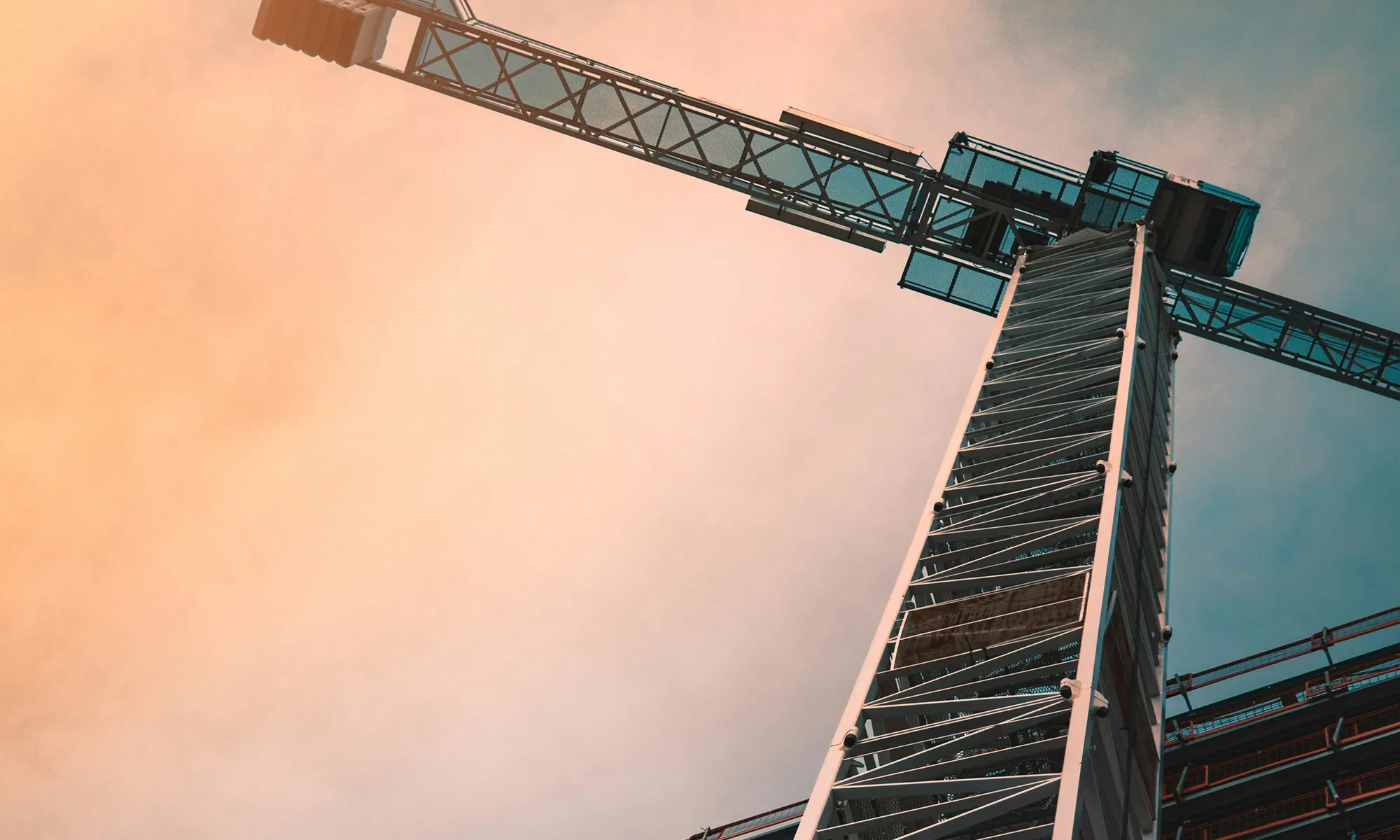 Low angle view of a construction crane tower against a sunset sky.