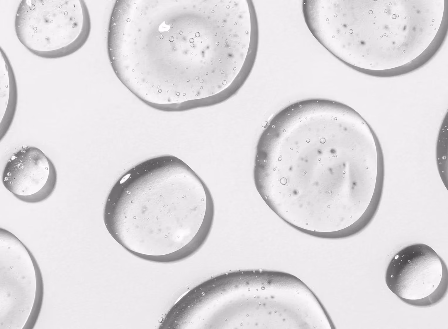 Multiple clear liquid droplets with small bubbles inside on a white background.