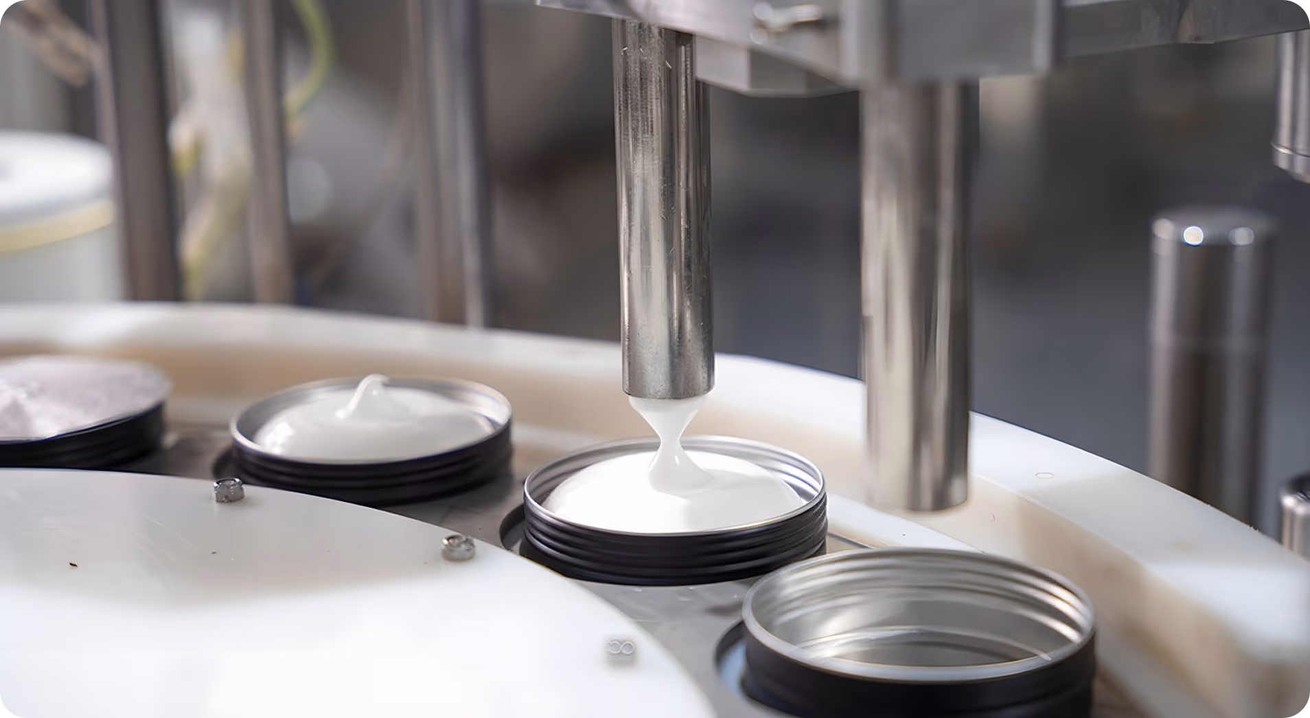 Machine dispensing white cream into open round containers on a production line.