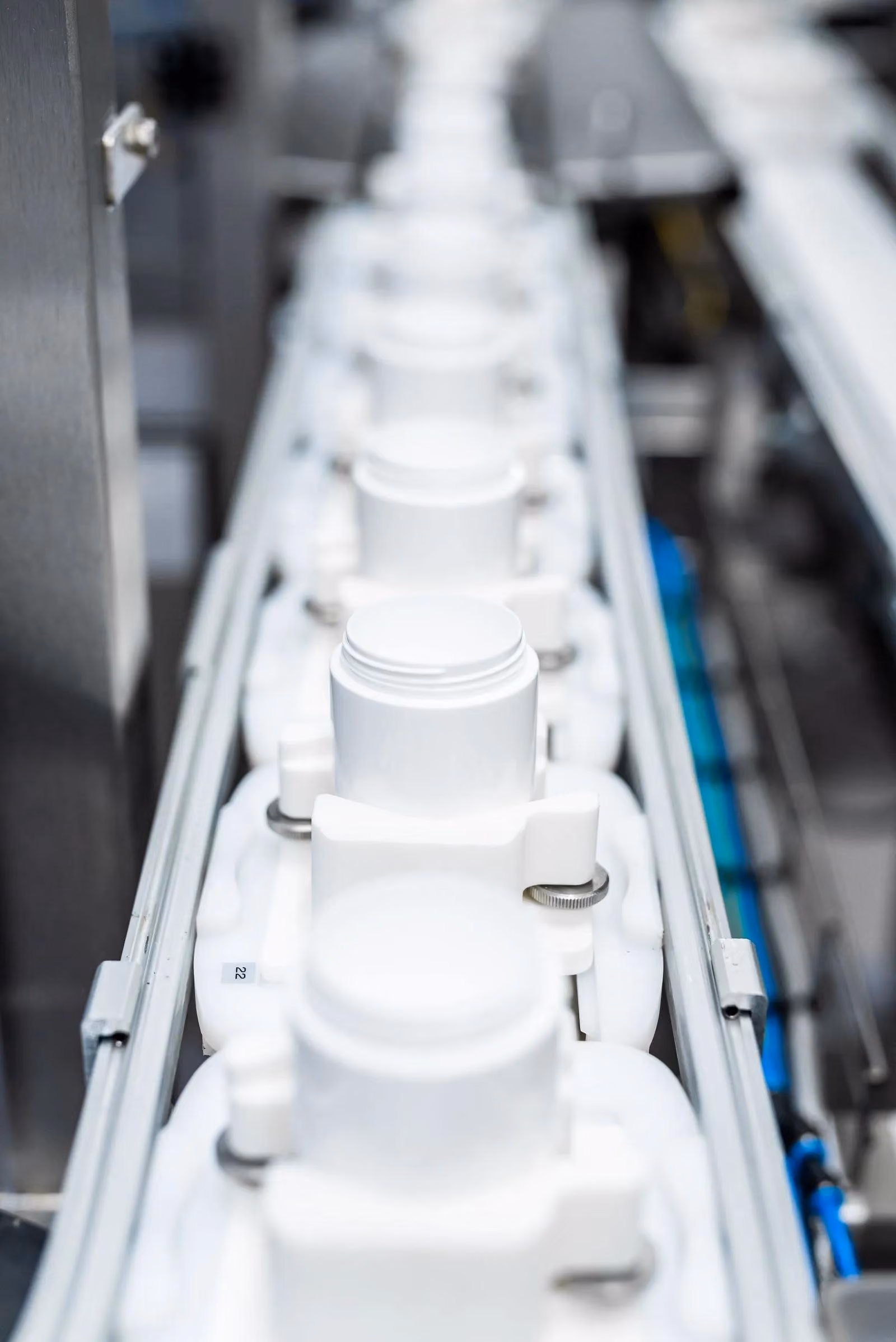 White plastic containers aligned in a row on an industrial production conveyor belt.