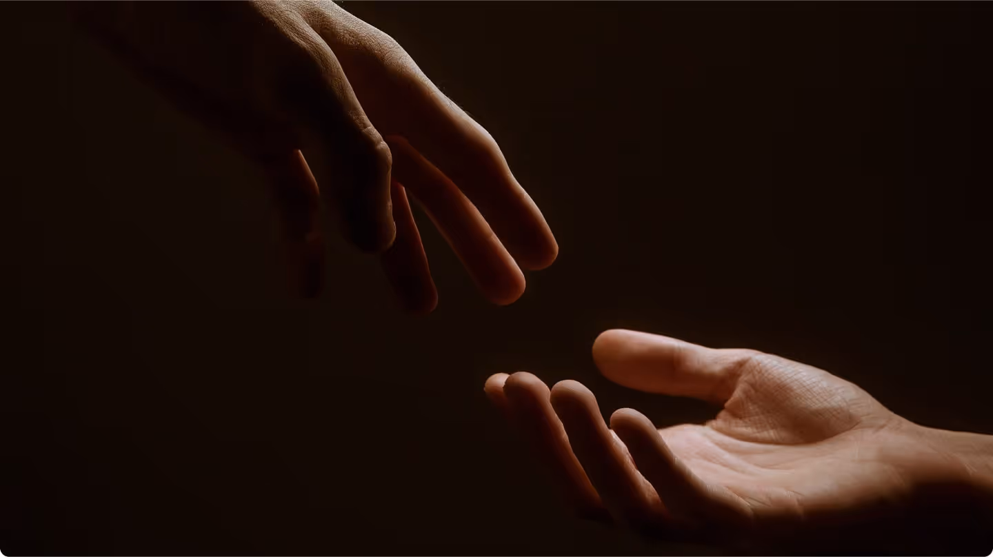 One hand reaching down to gently touch another open hand against a dark background.