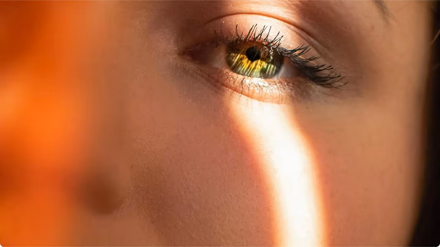 Close-up of a human eye with green and amber colors and sunlight casting a bright streak on the face.