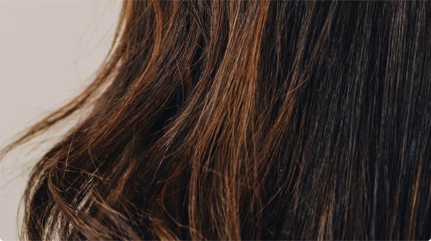 Close-up of long, dark brown hair with lighter brown highlights flowing against a beige background.
