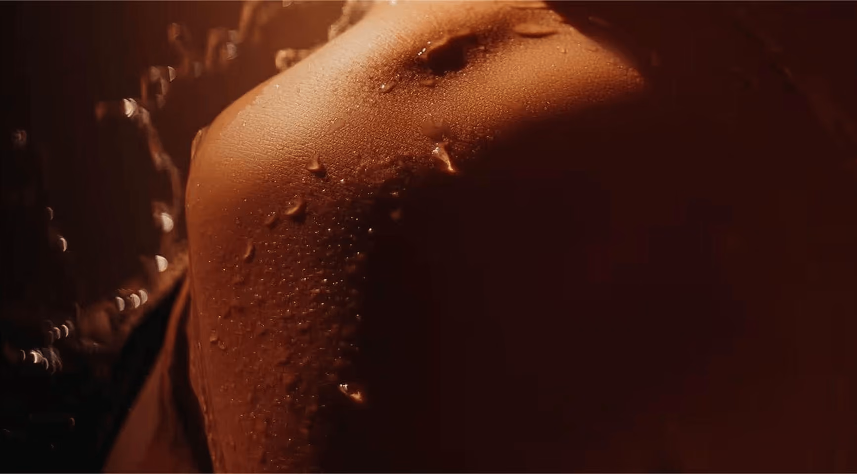 Close-up of a wet human back with water droplets and warm lighting.