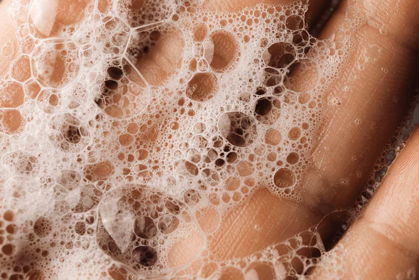 Close-up of soapy bubbles on a person's hand with visible skin texture.