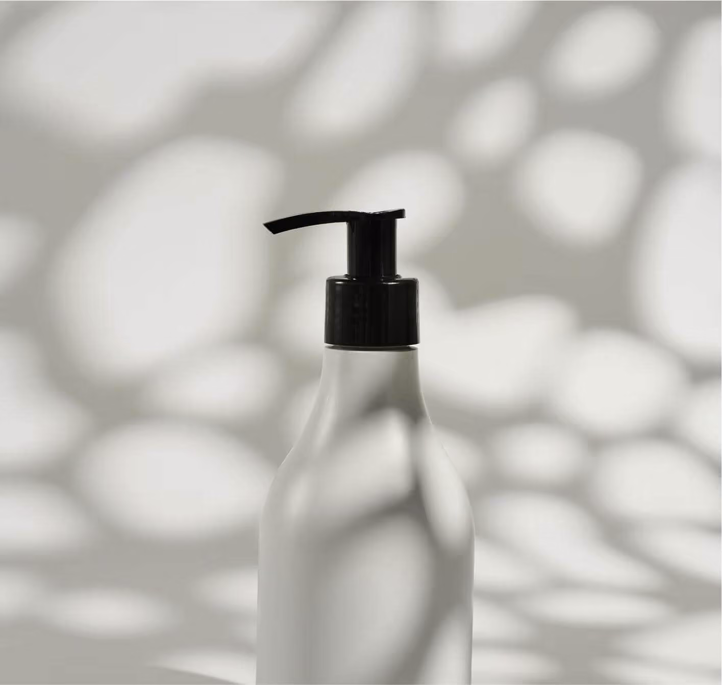 White bottle with black pump dispenser casting shadows on a light background.