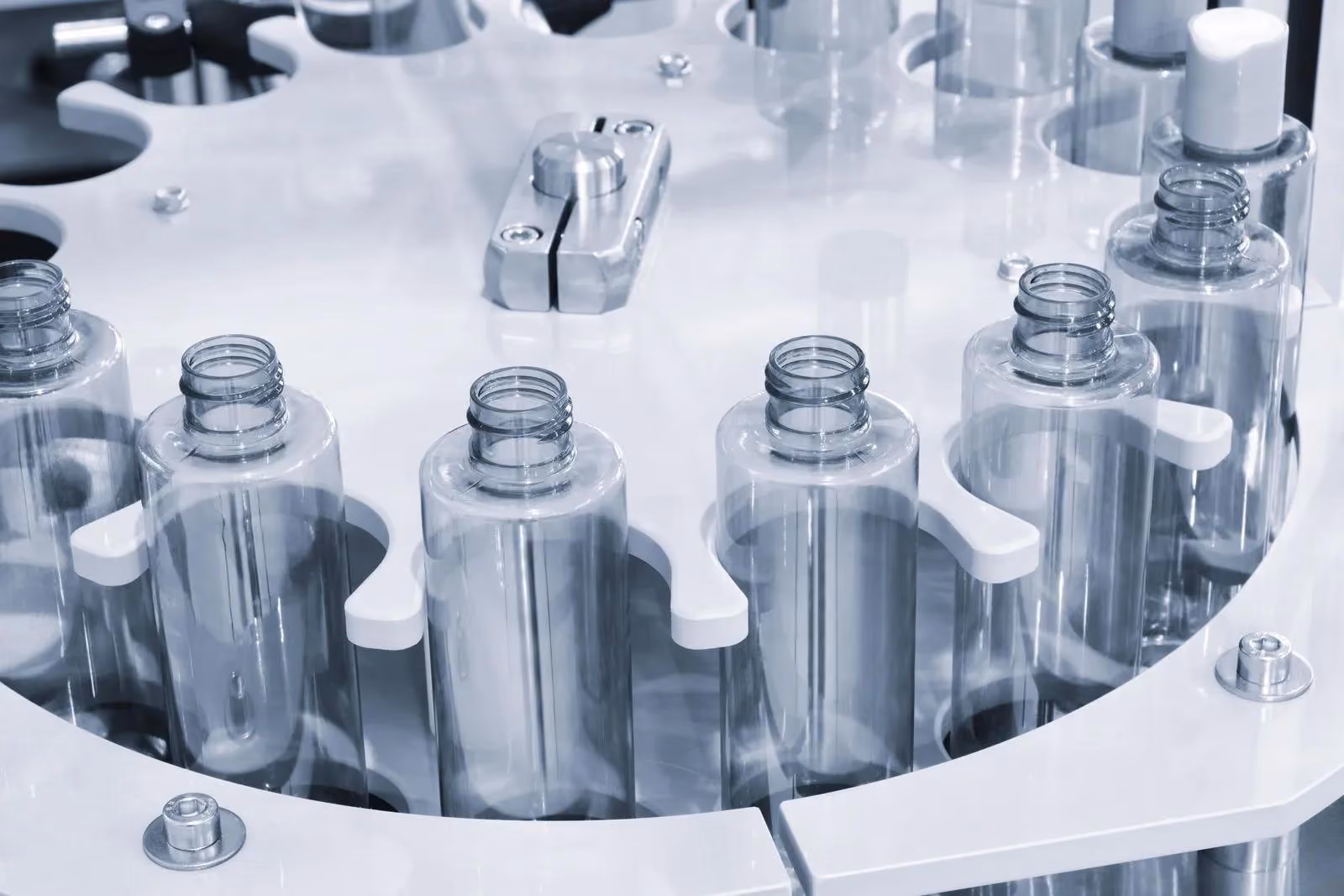 Clear plastic bottles aligned in a circular machine for filling or processing.
